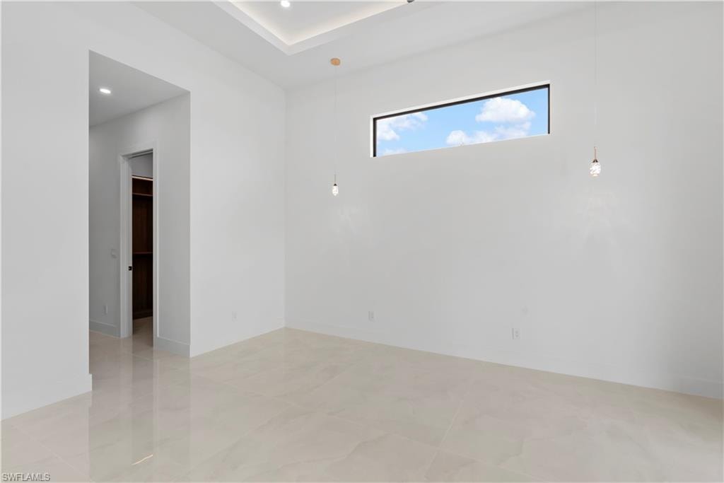 Recessed ceiling with integrated lighting, a rectangular transom window, pendant lighting, and polished tile flooring