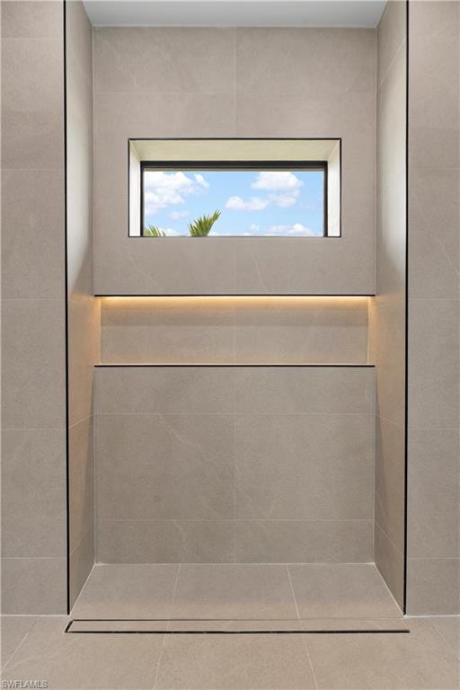 Tiled shower stall featuring a linear drain, recessed niche with accent lighting, and an integrated window