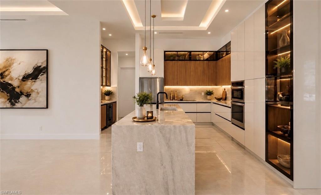 Central kitchen island with waterfall counter, integrated stainless steel appliances, recessed lighting, and wood-finish cabinetry