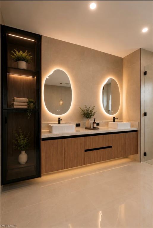 Dual vessel sinks with wall-mounted matte black faucets, integrated wood-finish cabinetry, illuminated floating mirrors, tiled walls, and ceramic flooring