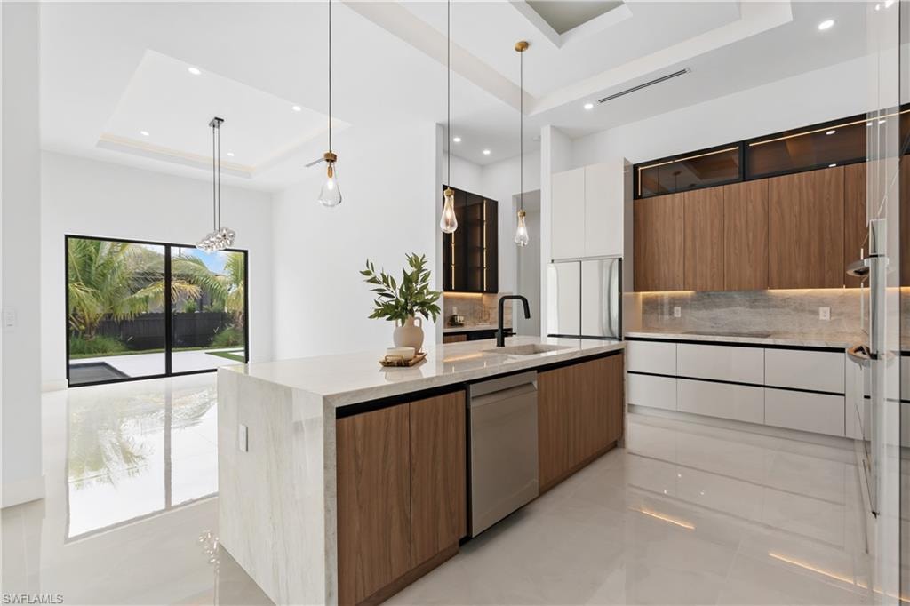 Spacious kitchen featuring a waterfall island, integrated stainless steel appliances, and wood-finish cabinetry