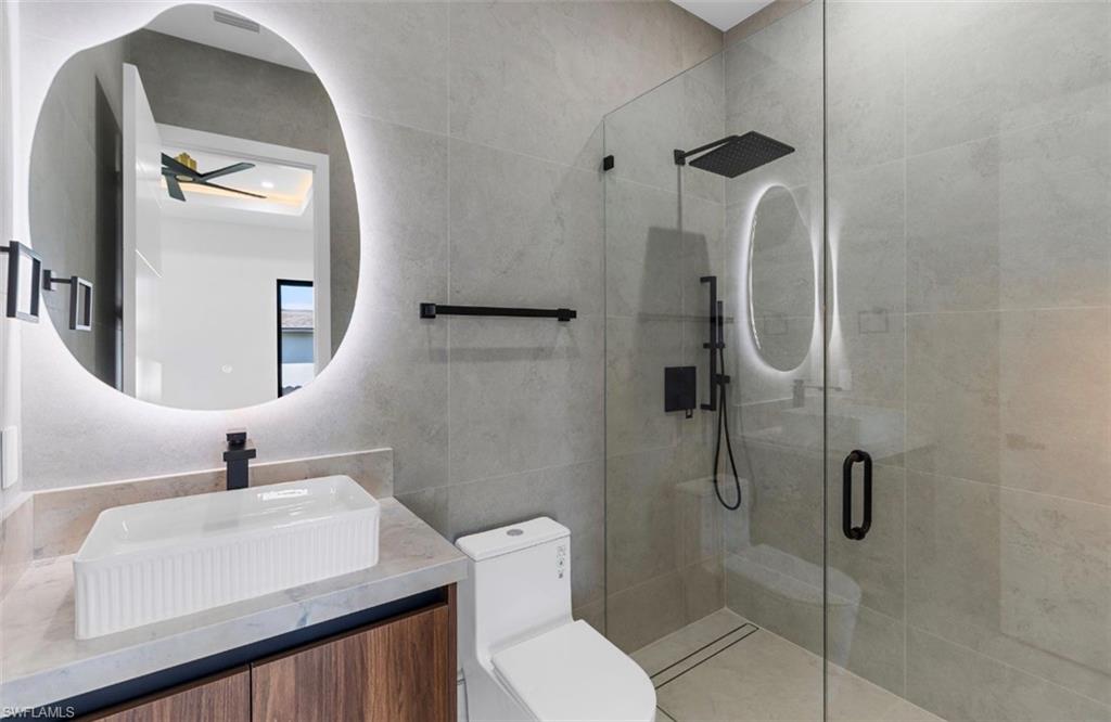 Backlit vanity mirror, vessel sink, wood-finish vanity, glass-enclosed shower, and matte black fixtures