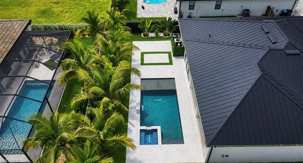 Modern metal roof, expansive concrete patio, rectangular swimming pool, integrated spa, and mature palm landscaping