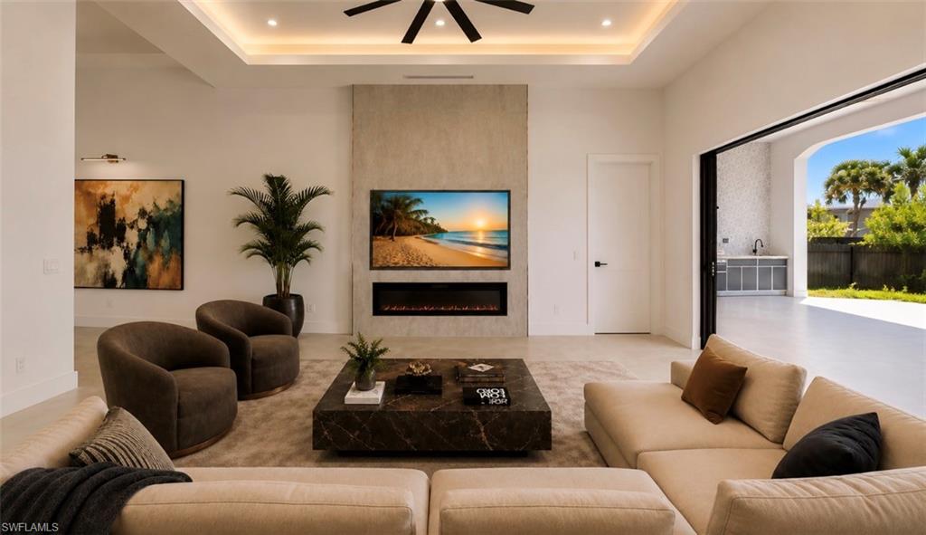 Recessed lighting, tray ceiling, ceiling fan, contemporary fireplace, and pocket sliding doors opening to an outdoor kitchen