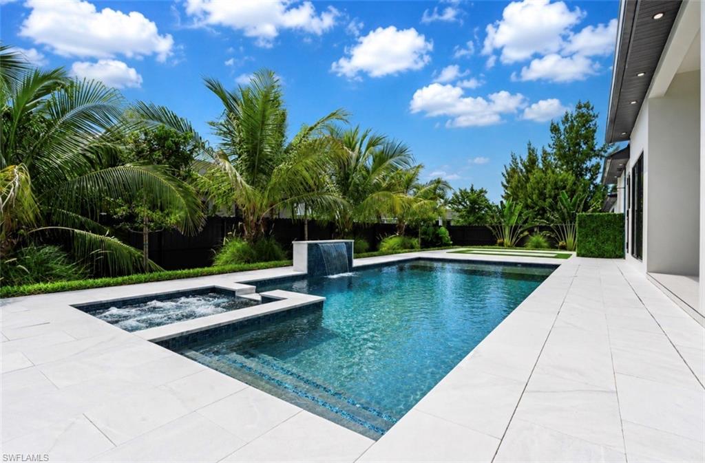 Pool and spa with integrated waterfall feature, surrounded by white tile decking and lush landscaping