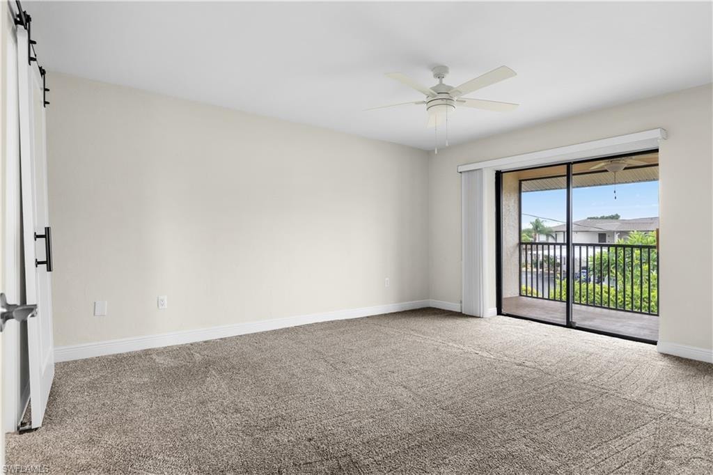 Neutral tone wall paint, textured carpet flooring, ceiling fan with integrated lighting, glass sliding door leading to an outdoor balcony
