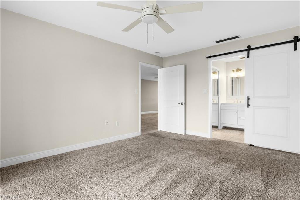 Carpeted room featuring a ceiling fan, white paneled doors, and a barn door entry to a bathroom with a double vanity