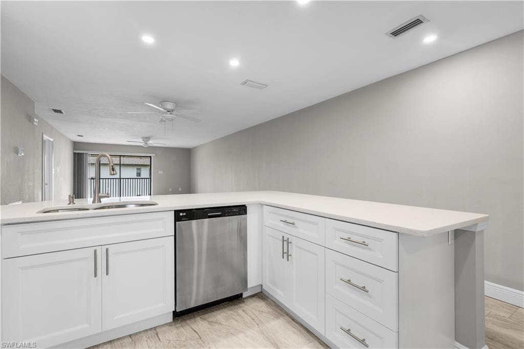 White cabinetry with brushed nickel hardware, stainless steel dishwasher, undermount sink with a gooseneck faucet, light-toned countertop, and recessed lighting