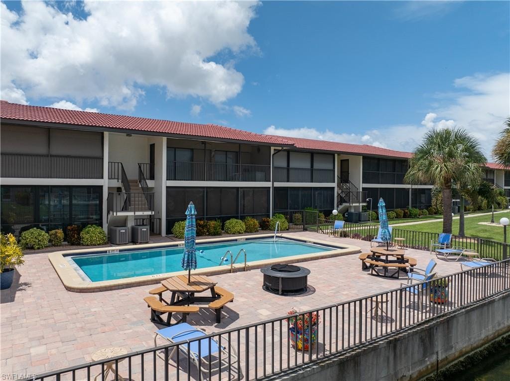 Community pool with paver decking, adjacent to a multi-story building with screened balconies and a red tile roof