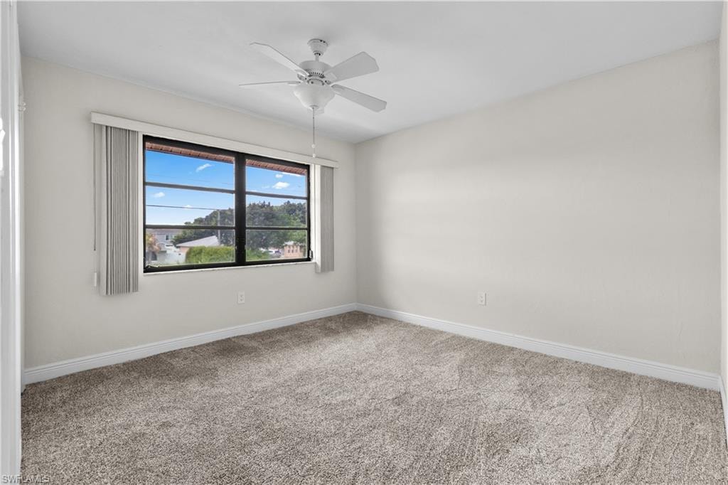 Neutral wall paint, textured carpet flooring, white ceiling fan with light kit, and a large window with vertical blinds