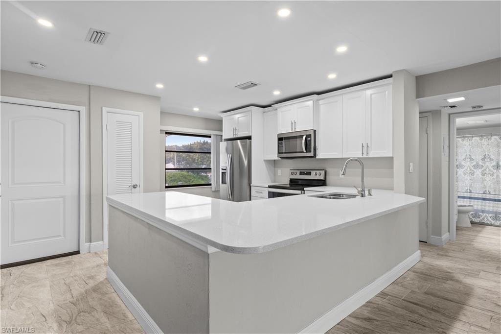 Modern kitchen featuring white cabinetry, quart countertops, stainless steel appliances, recessed lighting, and a peninsula with a curved countertop