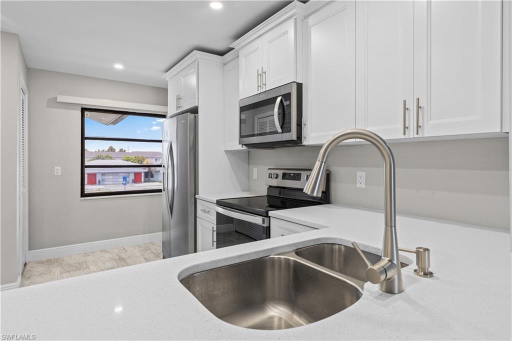 Kitchen featuring white cabinetry, stainless steel appliances, a double basin sink, and solid surface countertops