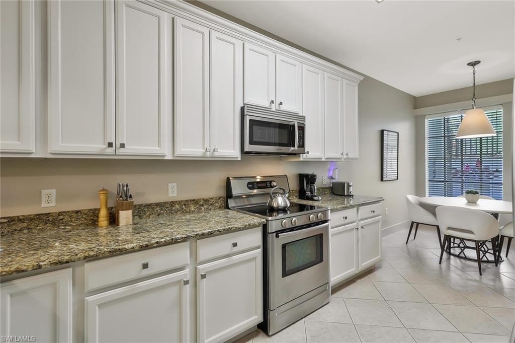 Kitchen with pendant lighting, light tile patterned floors, white cabinets, dark stone countertops, and stainless steel appliances