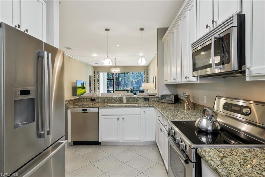 Kitchen with light tile patterned floors, white cabinets, a sink, stainless steel appliances, and pendant lighting