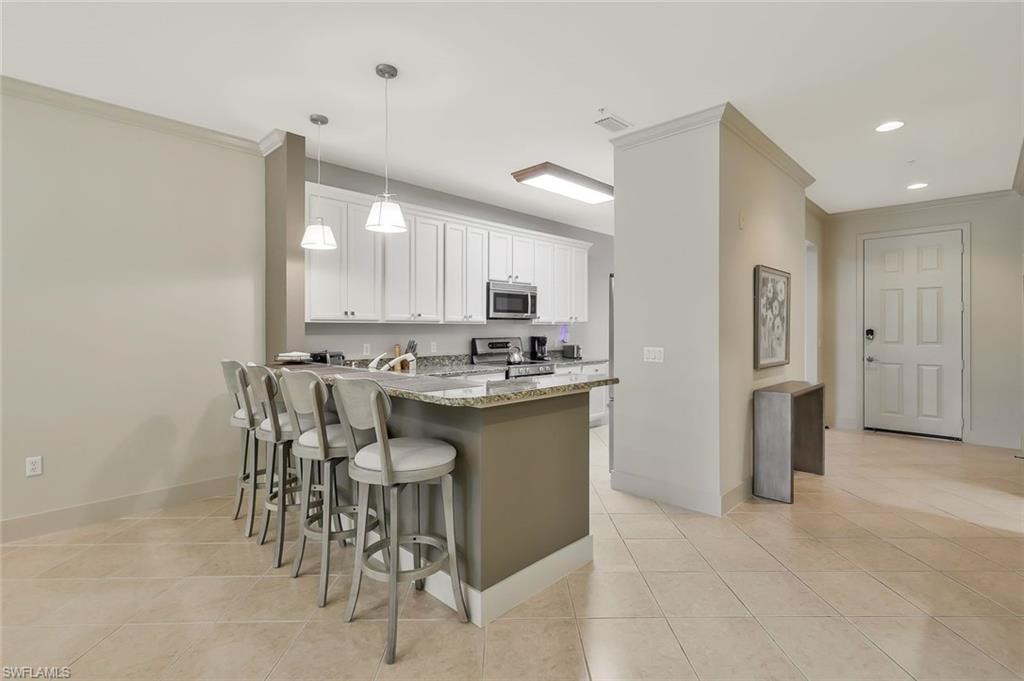 Kitchen with a peninsula, a kitchen bar, white cabinetry, light stone countertops, and stainless steel appliances