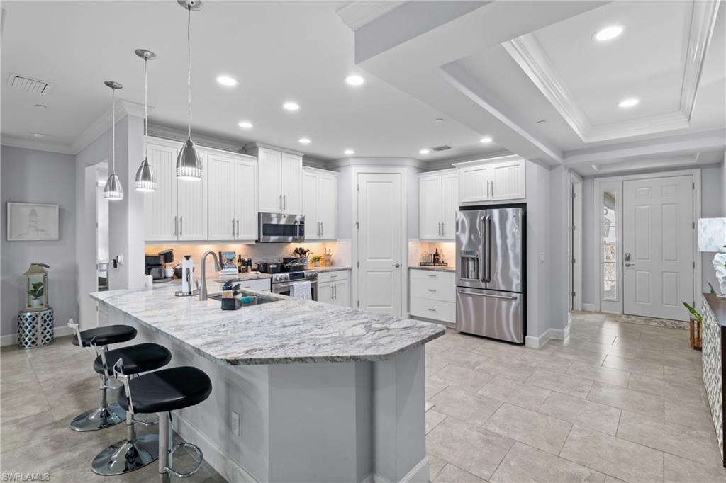 Modern kitchen featuring white shaker cabinetry, stainless steel appliances, a large island with a stone countertop, and recessed lighting