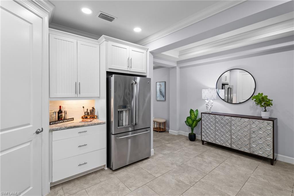 Integrated stainless steel refrigerator, white shaker-style cabinetry, granite countertop, subway tile backsplash, and recessed lighting