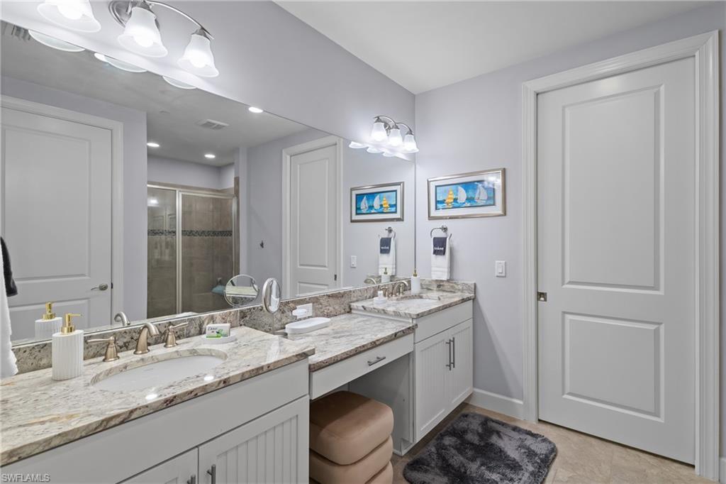 Dual vanity with stone countertops, undersink cabinetry, and a full-width mirror