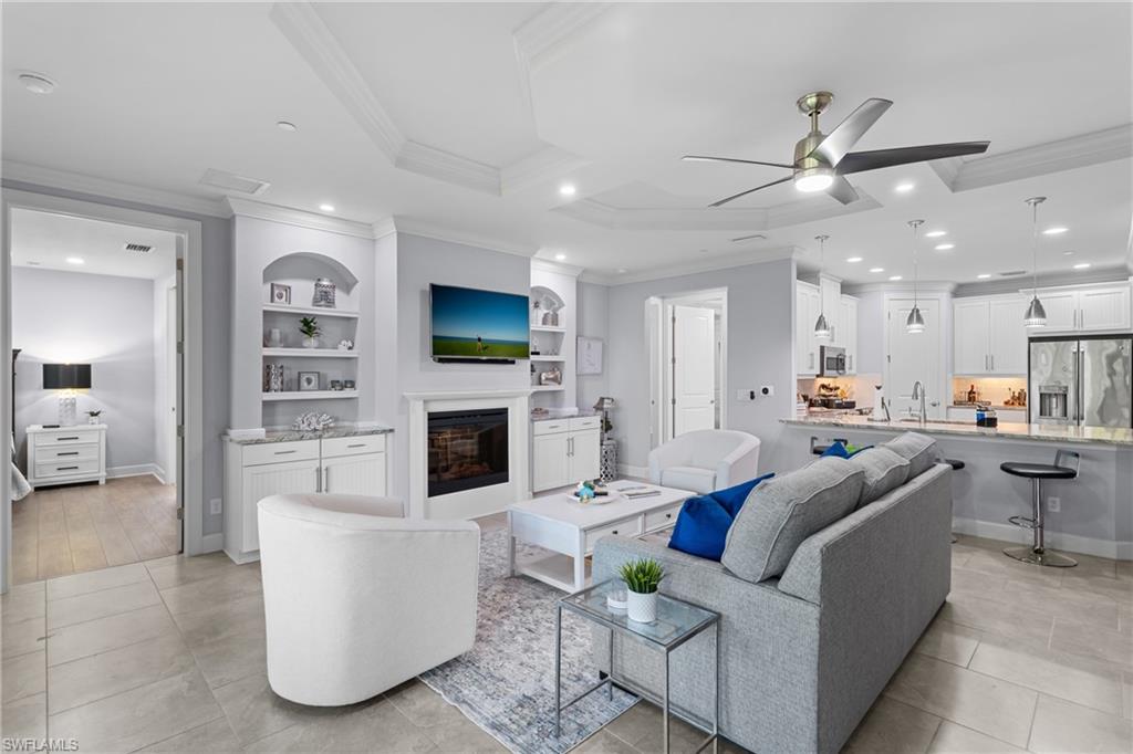 Open-concept living space featuring a tray ceiling, recessed lighting, tile flooring, and a built-in fireplace with shelving