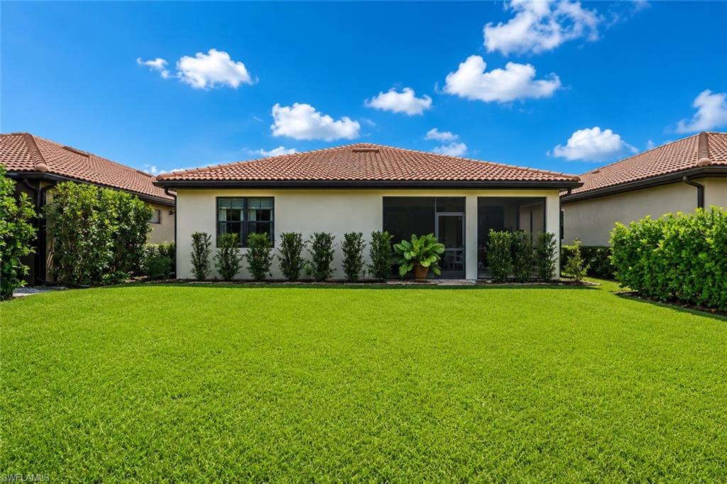 Expansive green lawn with mature landscaping, stucco exterior, tiled roof, and a screened lanai