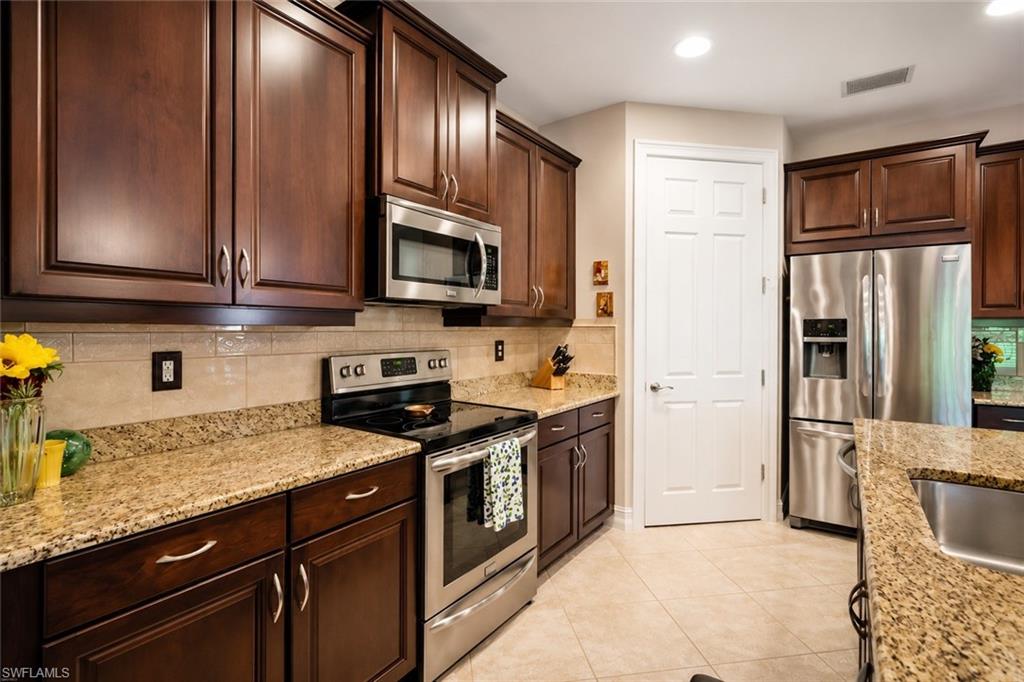 Kitchen featuring dark wood cabinetry, stainless steel appliances, light granite countertops, and a kitchen island with a stainless steel sink