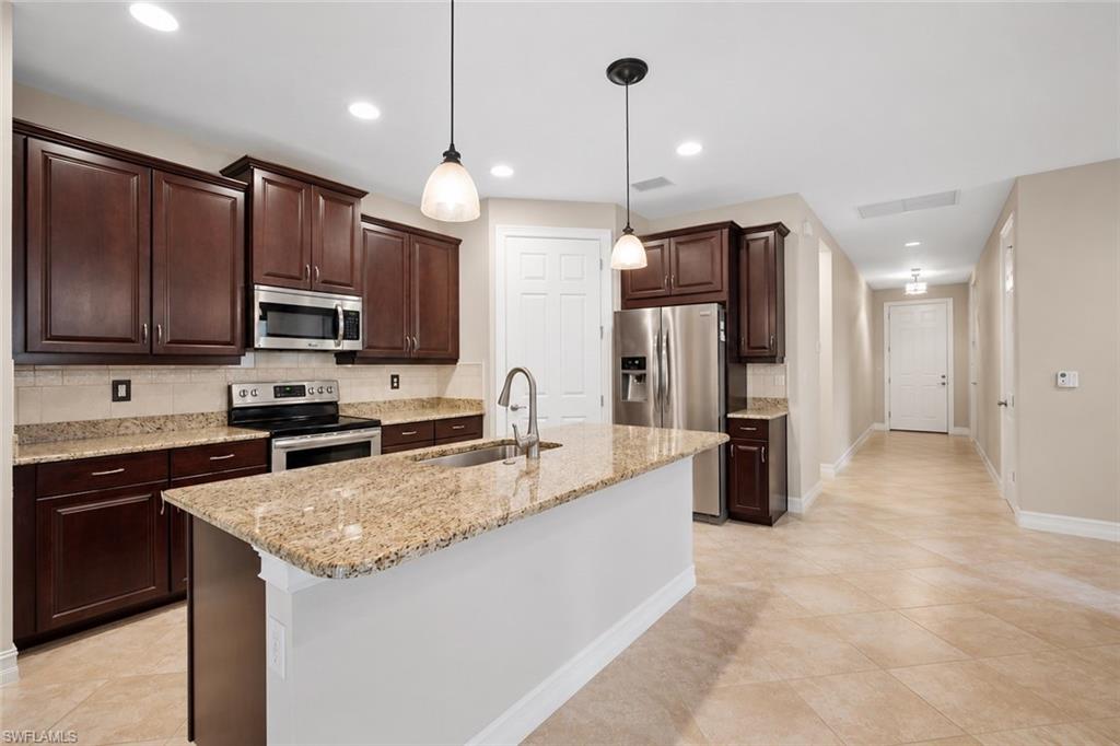 Tiled roof residence featuring a paver driveway, an attached garage, and mature landscaping