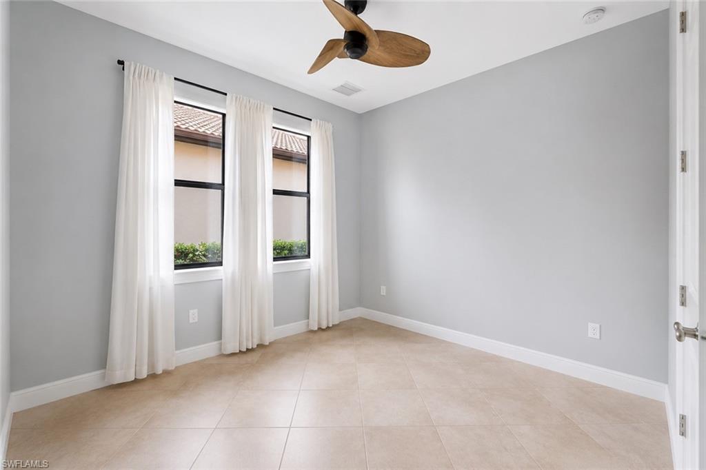 Recessed lighting, ceiling fan with wood-finish blades, three windows with white drapes, neutral tile flooring, and light gray wall paint