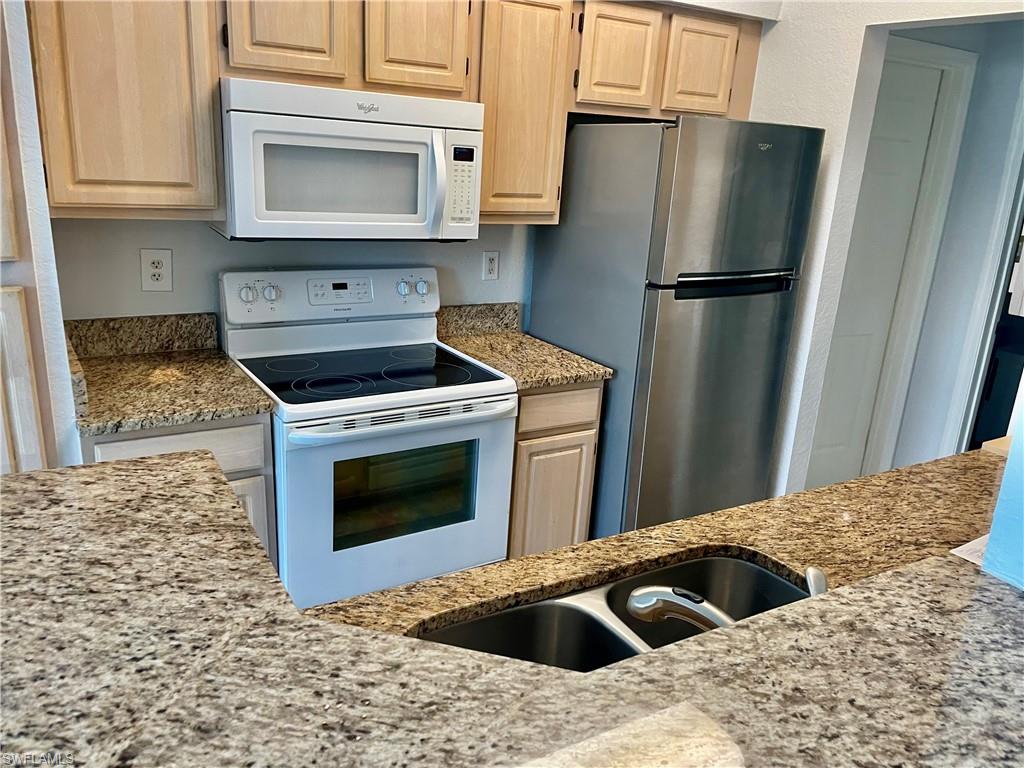 Kitchen featuring light stone counters, light brown cabinetry, white appliances, and sink