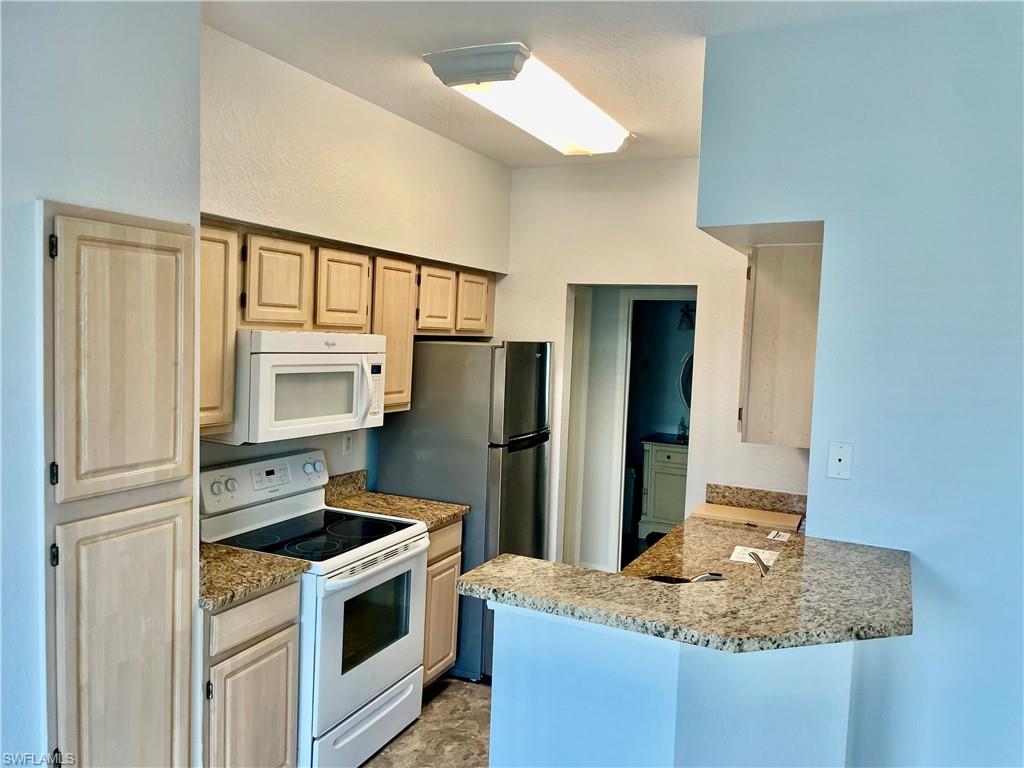 Kitchen featuring light brown cabinetry, kitchen peninsula, white appliances, and light stone countertops