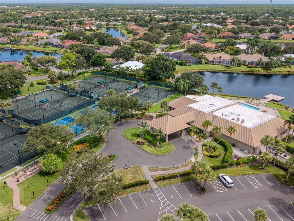 Community club building with a swimming pool, multiple tennis courts, pickleball courts, and a parking area, surrounded by a landscaped entrance and water features
