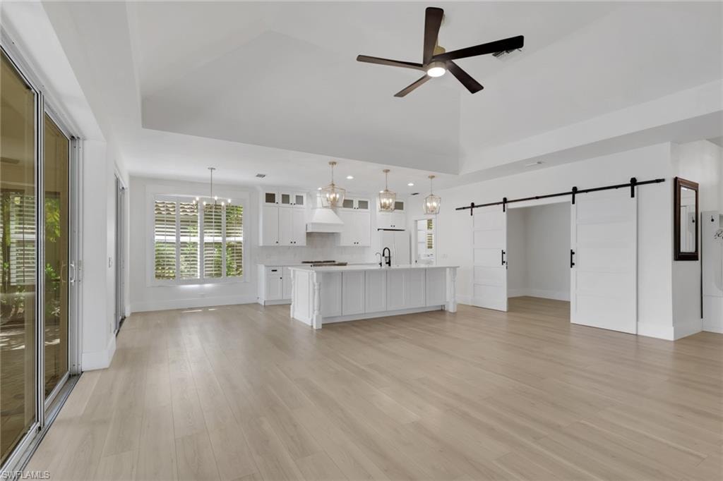 Vaulted ceiling, wood-finish flooring, kitchen island with built-in cabinetry, sliding barn doors, and sliding glass doors