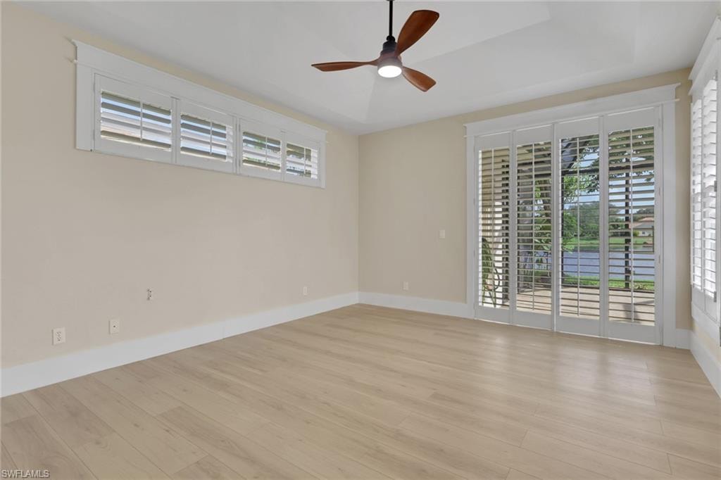 Wood-finish flooring, white plantation shutters, ceiling fan with light fixture, tray ceiling, and sliding glass doors
