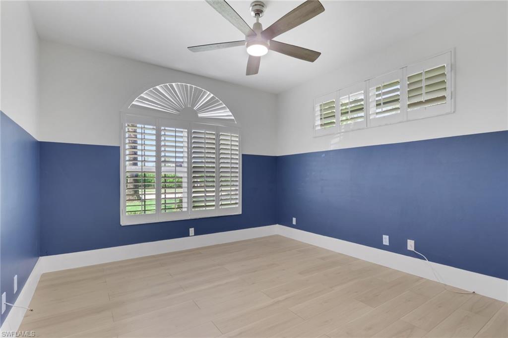 Arched window with plantation shutters, additional transom windows, wood-finish flooring, and a ceiling fan with integrated lighting