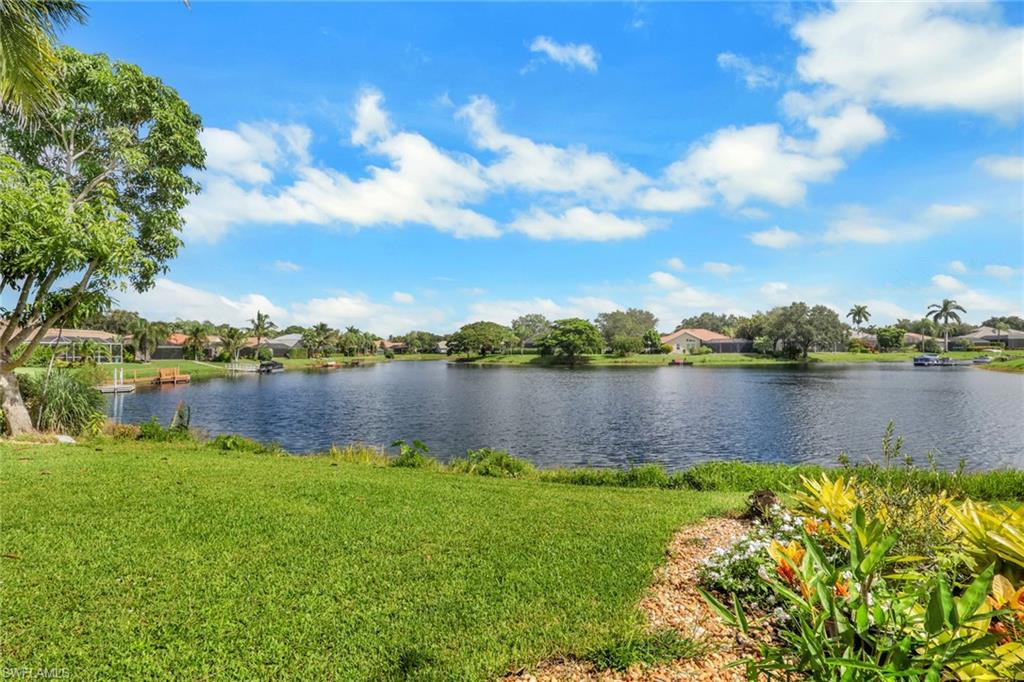 Waterfront property featuring a landscaped garden bed, manicured lawn, and mature trees