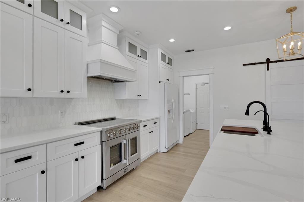 Gourmet kitchen featuring white shaker cabinetry, an integrated range hood, a professional-grade stainless steel range, and light-toned wood-finish flooring