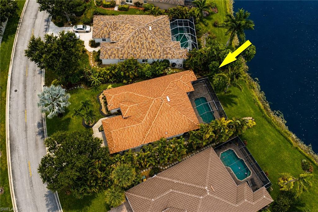 Waterfront property featuring a red tile roof, screened pool enclosure, and mature landscaping
