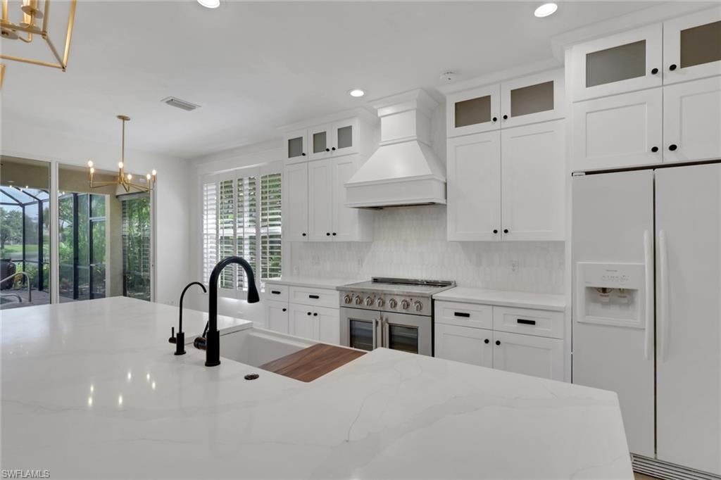 Expansive kitchen island with a built-in sink and matte black faucet, full-height white cabinetry, stainless steel range, and a tile backsplash
