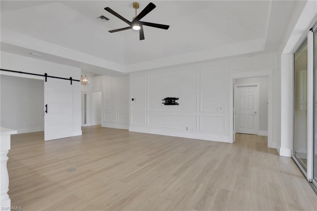 Recessed tray ceiling, contemporary ceiling fan, wood-finish flooring, white panel molding, and a sliding barn door