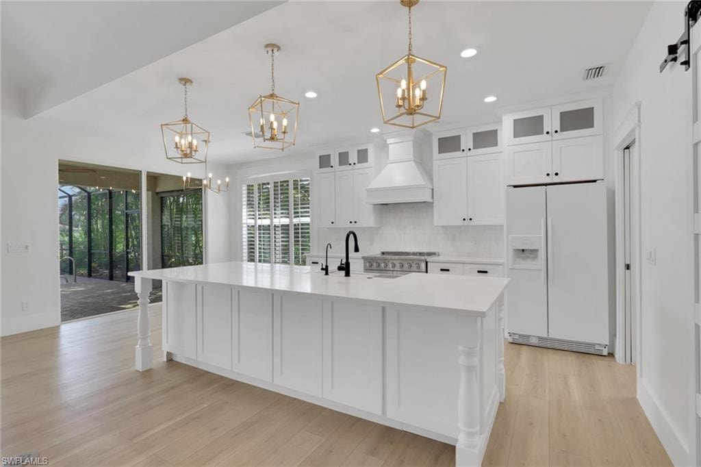 Expansive kitchen island with substantial turned legs, white cabinetry, quartz countertops, and wood-finish flooring