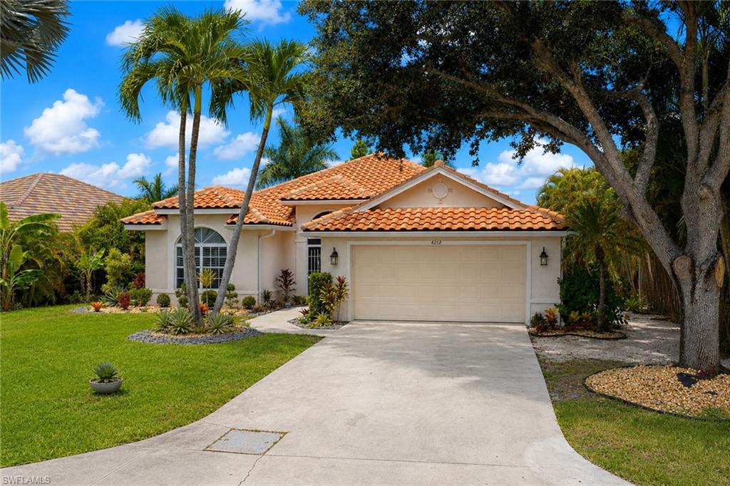 Stucco exterior residence featuring a barrel tile roof, arched transom window, attached garage, and mature landscaping