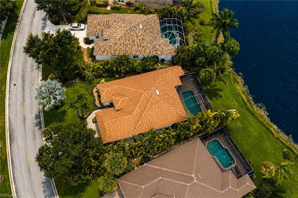 Waterfront property with a terracotta tile roof, screened swimming pool, and lush landscaping