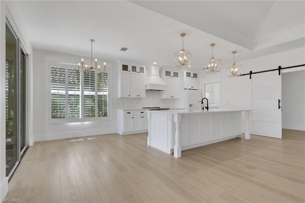 Spacious open-concept kitchen featuring a large central island, white cabinetry, integrated range hood, and light wood-finish flooring