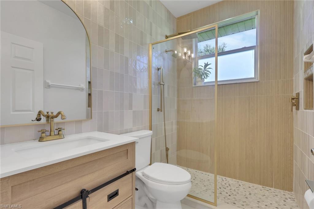 Walk-in shower with clear glass enclosure, natural pebble flooring, and textured wall tile