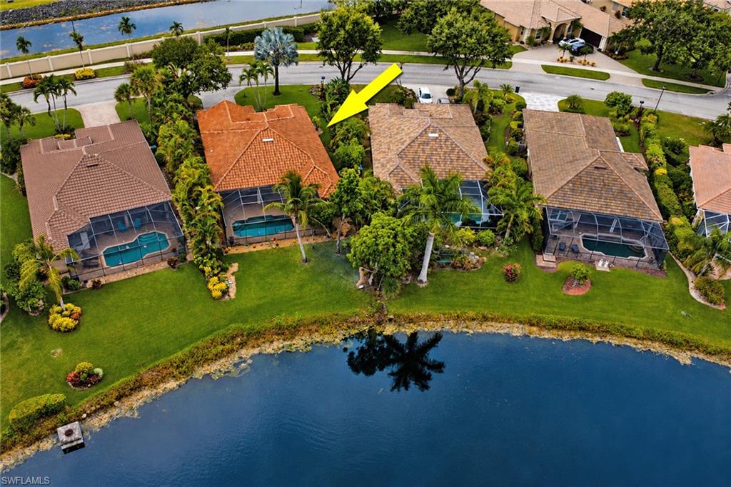 Waterfront property featuring a screened-in pool, manicured lawn, and mature landscaping