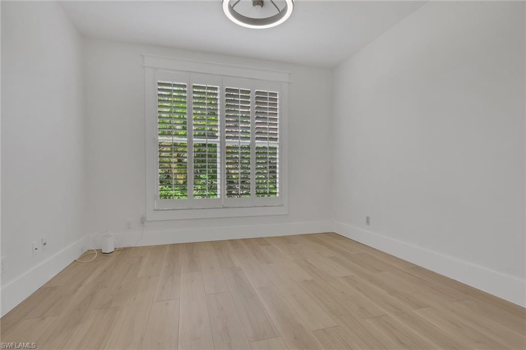 Light wood-finish flooring with white baseboards, window with white plantation shutters, and a modern ceiling light fixture