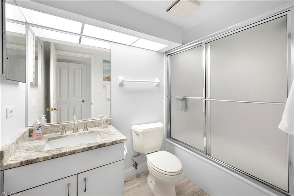Bathroom featuring combined bath / shower with glass door, vanity, and light wood-style flooring