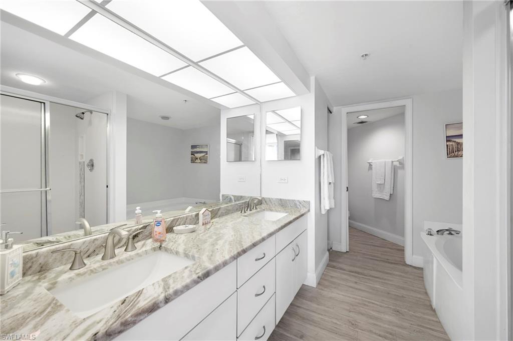 Bathroom with a bath, double vanity, a stall shower, and light wood finished floors