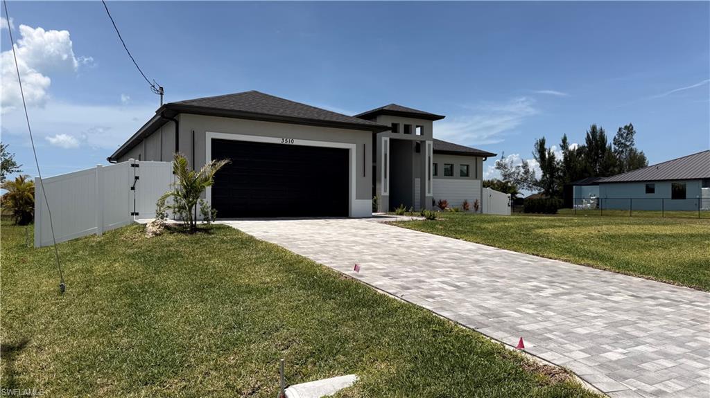 Modern architectural style featuring an attached garage, a paver driveway, and a white privacy fence