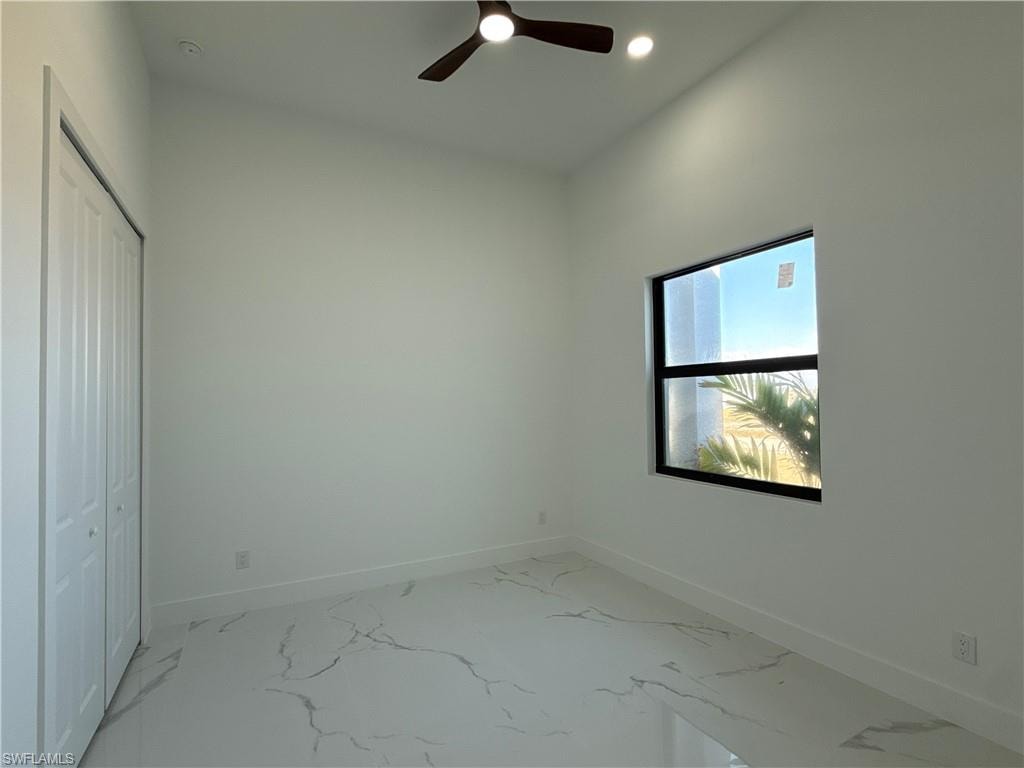 White tile flooring with grey veining, white walls, black-framed window, bi-fold closet doors, and a ceiling fan