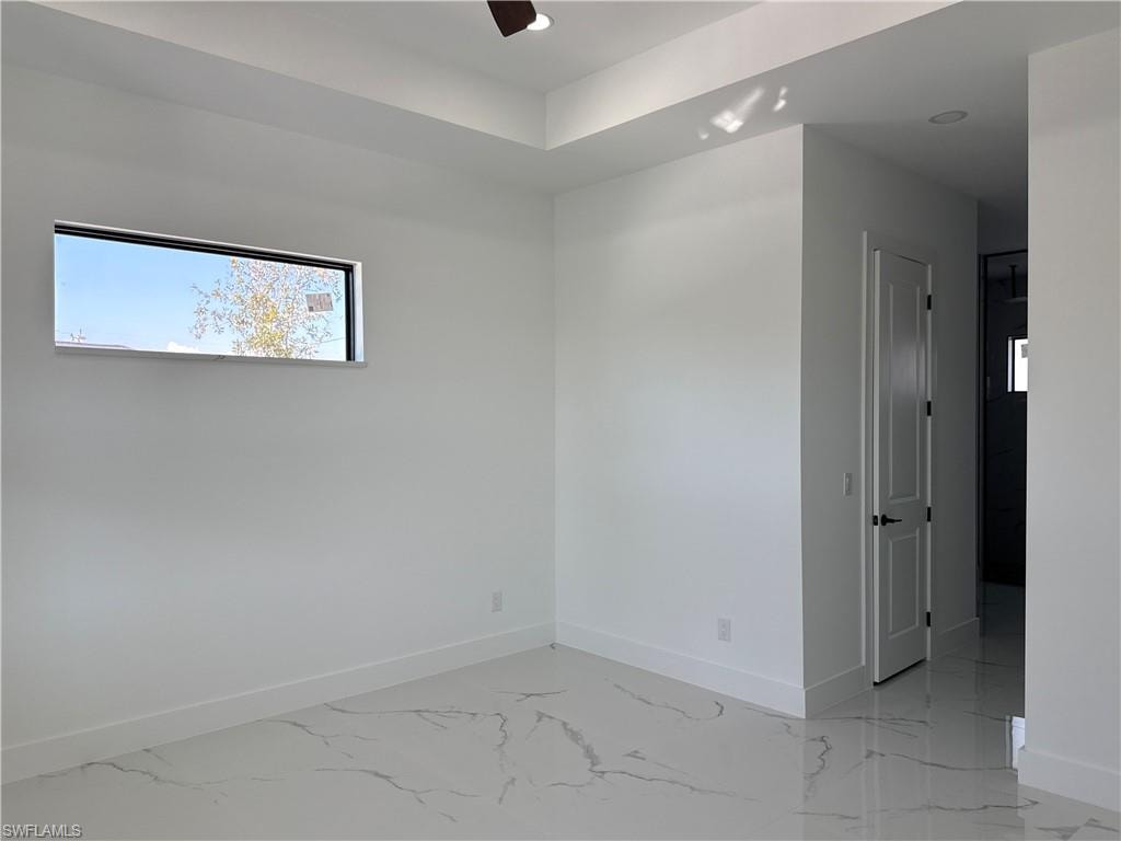 Tray ceiling, recessed lighting, rectangular window, paneled interior door with dark hardware, and marble-look tile flooring